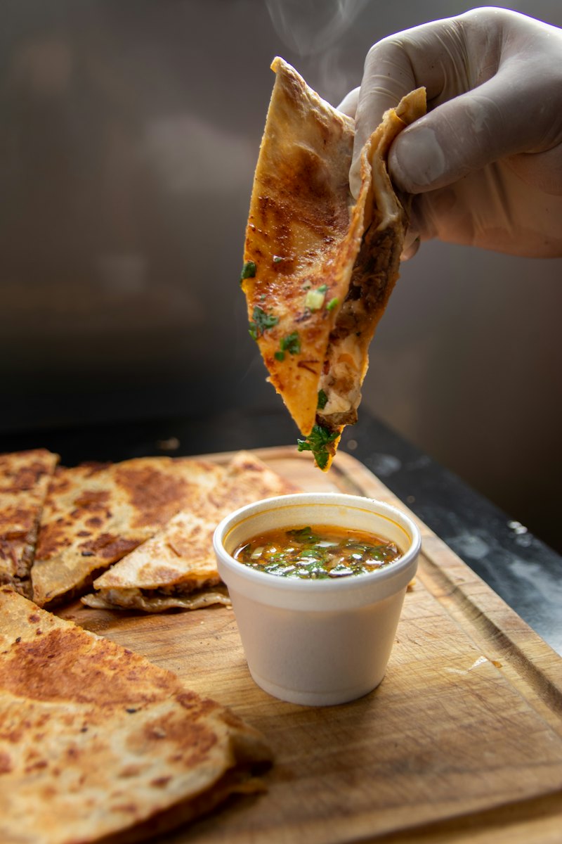 A crisp birria taco dipped into a cup of consommé
