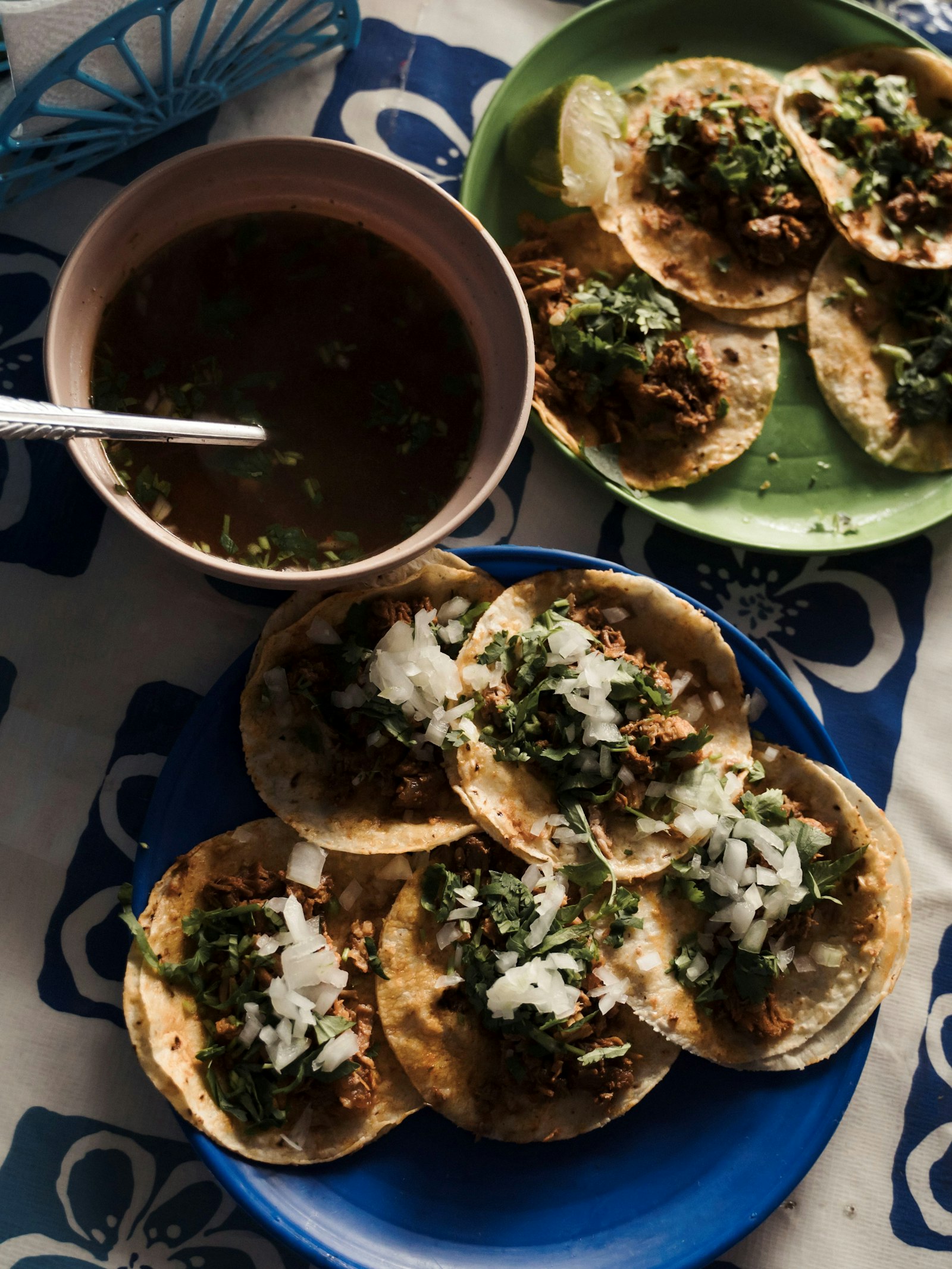 Plates of birria tacos with onion and cilantro beside a bowl of consommé